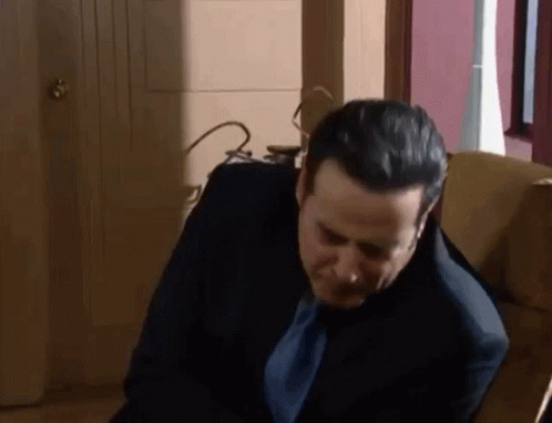 A Man In A Suit And Tie Is Sitting In A Chair And Looking Down . GIF