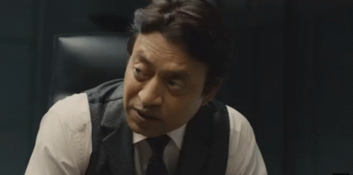 A Man In A Suit And Tie Is Sitting In A Chair And Talking To Someone . GIF