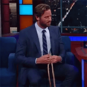 A Man In A Suit And Tie Is Sitting In A Chair And Tying A Rope . GIF
