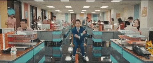 A Man In A Suit And Tie Is Sitting In A Chair In An Office Surrounded By People . GIF