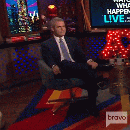 Man In Suit Sitting In Front Of Bravo Sign GIF