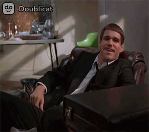 A Man In A Suit And Tie Is Sitting In A Chair With A Briefcase Next To Him .. GIF