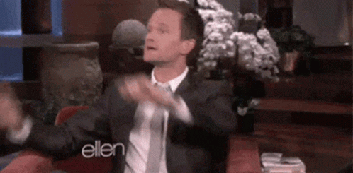 A Man In A Suit And Tie Is Sitting In A Chair With His Arms Outstretched On A Talk Show . GIF