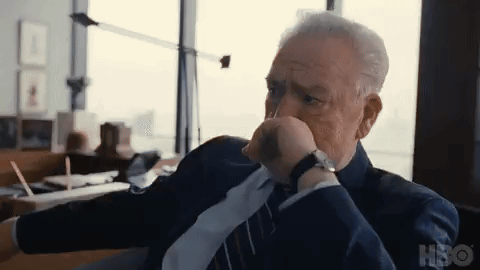 A Man In A Suit And Tie Is Sitting In A Chair With His Hand On His Chin . GIF