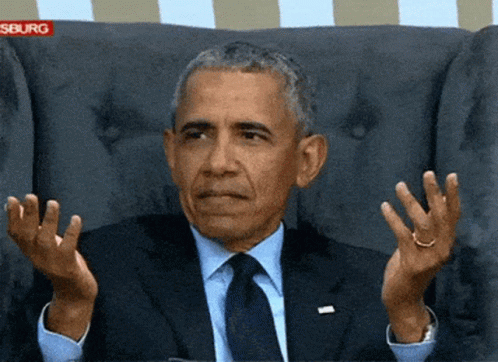 A Man In A Suit And Tie Is Sitting In A Chair With His Hands In The Air GIF