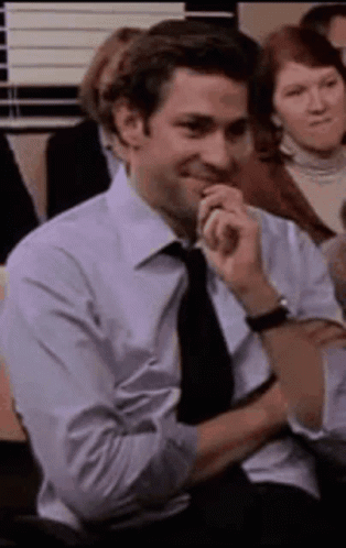 A Man In A Suit And Tie Is Sitting In A Chair With His Hands On His Chin . GIF
