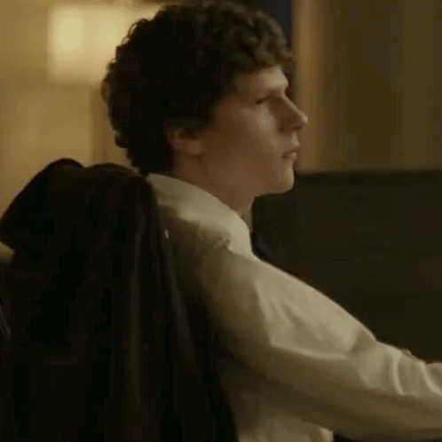 A Man In A Suit And Tie Is Sitting In A Chair With His Jacket On His Back . GIF