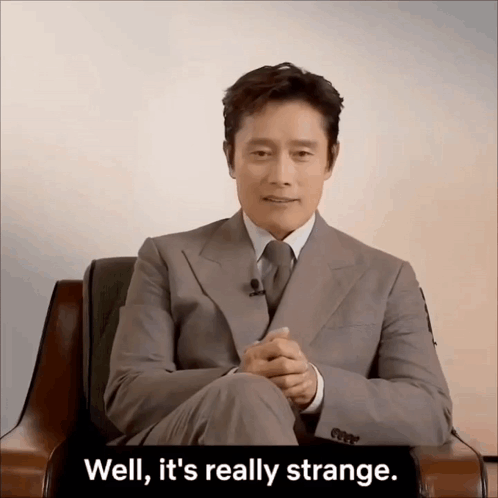 A Man In A Suit And Tie Is Sitting In A Chair With The Words Well It 'S Really Strange Behind Him GIF