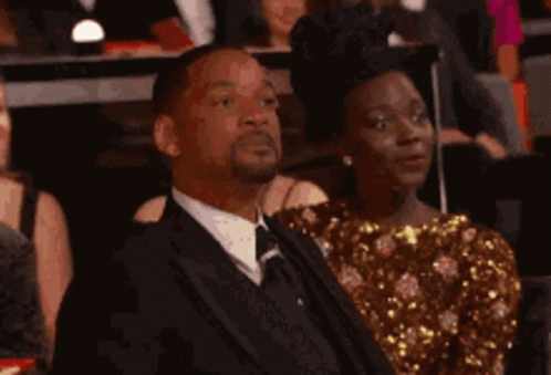 A Man In A Suit And Tie Is Sitting In A Crowd Of People . GIF