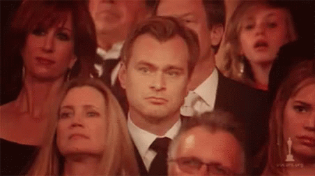 A Man In A Suit And Tie Is Sitting In A Crowd Of People Watching A Movie . GIF