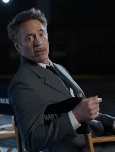 A Man In A Suit And Tie Is Sitting In A Director 'S Chair That Says Pascal On It GIF