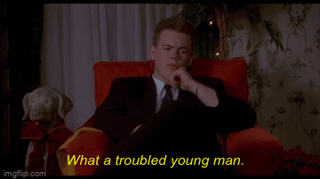 A Man In A Suit And Tie Is Sitting In A Red Chair With The Words What A Troubled Young Man Behind Him GIF