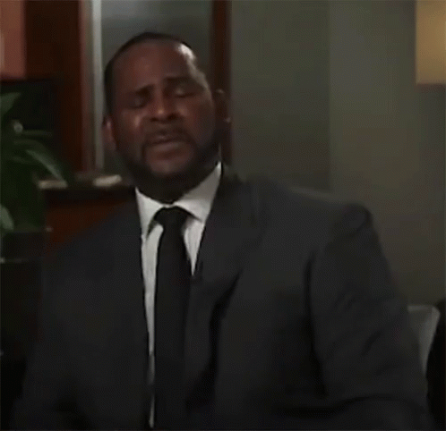 A Man In A Suit And Tie Is Sitting In A Room . GIF