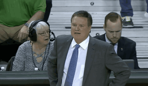 A Man In A Suit And Tie Is Sitting In A Stadium GIF