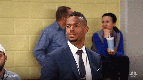 A Man In A Suit And Tie Is Sitting In A Waiting Room With Other People . GIF