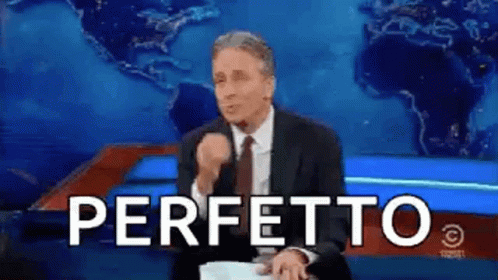 A Man In A Suit And Tie Is Sitting In Front Of A Blue Background With The Word Perfetto Written In White Letters . GIF