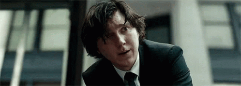 A Man In A Suit And Tie Is Sitting In Front Of A Building . GIF