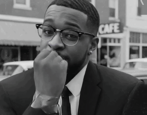 A Man In A Suit And Tie Is Sitting In Front Of A Cafe Sign GIF