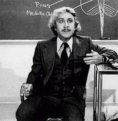 A Man In A Suit And Tie Is Sitting In Front Of A Chalkboard That Says Pong Medulla GIF