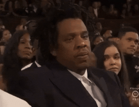 A Man In A Suit And Tie Is Sitting In Front Of A Crowd And A Sign That Says Rep On It GIF