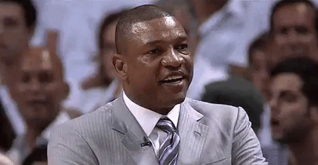 A Man In A Suit And Tie Is Sitting In Front Of A Crowd Of People . GIF