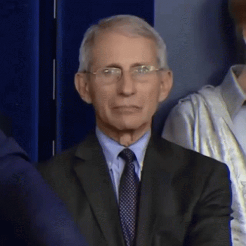 A Man In A Suit And Tie Is Sitting In Front Of A Crowd . GIF