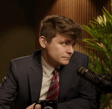 A Man In A Suit And Tie Is Sitting In Front Of A Microphone And Holding A Mug That Says ' Washington ' GIF