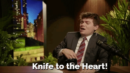 A Man In A Suit And Tie Is Sitting In Front Of A Microphone And Says Knife To The Heart GIF