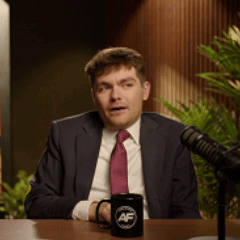 A Man In A Suit And Tie Is Sitting In Front Of A Microphone With A Mug That Says Af On It GIF