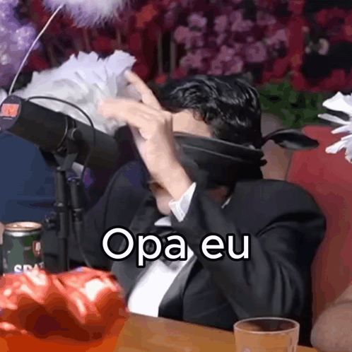 A Man In A Suit And Tie Is Sitting In Front Of A Microphone With The Words Opa Eu Written On The Screen GIF