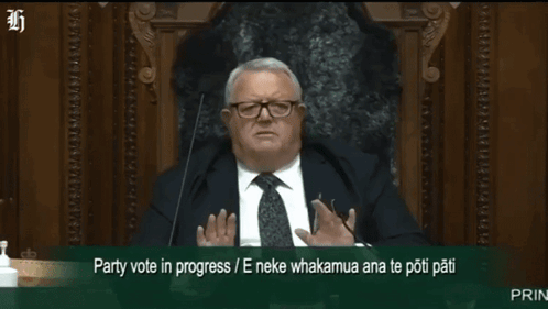 A Man In A Suit And Tie Is Sitting In Front Of A Microphone With The Words Party Vote In Progress Written Below Him GIF