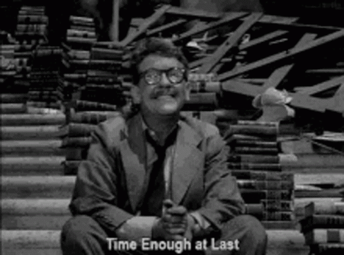 A Man In A Suit And Tie Is Sitting In Front Of A Pile Of Books And Says `` Time Enough At Last '' . GIF
