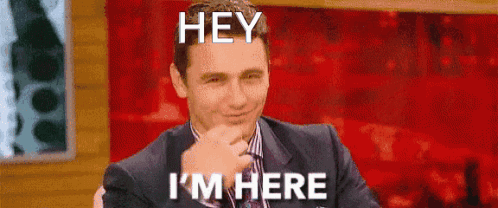 A Man In A Suit And Tie Is Sitting In Front Of A Red Background And Making A Funny Face . GIF