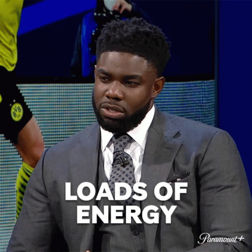A Man In A Suit And Tie Is Sitting In Front Of A Screen That Says Loads Of Energy GIF