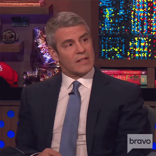 Man In Suit Sitting In Front Of Bravo Sign GIF
