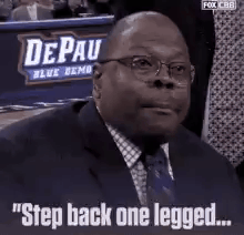 A Man In A Suit And Tie Is Sitting In Front Of A Sign That Says `` Step Back One Legged `` . GIF