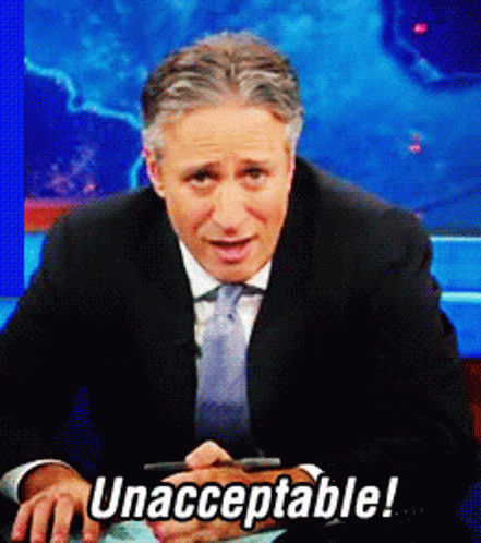 A Man In A Suit And Tie Is Sitting In Front Of A Sign That Says Unacceptable GIF