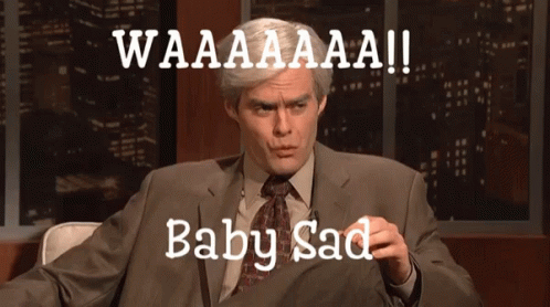 A Man In A Suit And Tie Is Sitting In Front Of A Sign That Says Waaaaaaa Baby Sad GIF