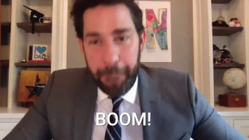 A Man In A Suit And Tie Is Sitting In Front Of A Wall With A Picture Of A Letter N On It . GIF