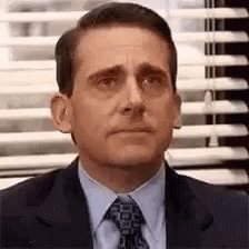 A Man In A Suit And Tie Is Sitting In Front Of A Window . GIF