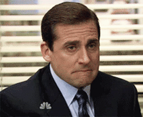 A Man In A Suit And Tie Is Sitting In Front Of A Window With Blinds . GIF