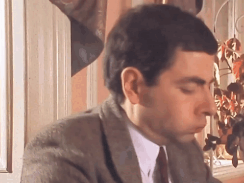A Man In A Suit And Tie Is Sitting In Front Of A Window With His Eyes Closed . GIF