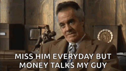 A Man In A Suit And Tie Is Sitting In Front Of A Wooden Wall And Talking About Money . GIF