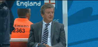 A Man In A Suit And Tie Is Sitting In Front Of An England Sign GIF