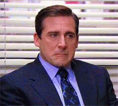 A Man In A Suit And Tie Is Sitting In Front Of Blinds GIF