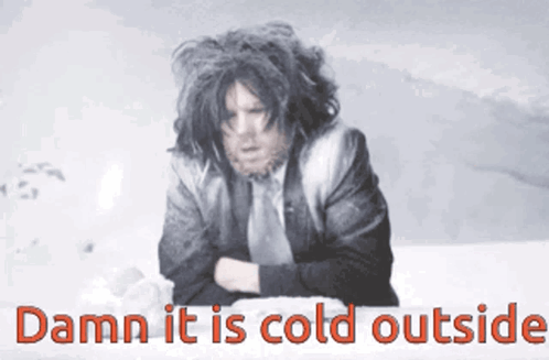 A Man In A Suit And Tie Is Sitting In The Snow With The Words Damn It Is Cold Outside GIF