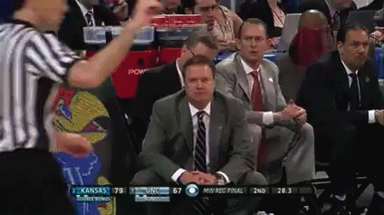 A Man In A Suit And Tie Is Sitting In The Stands Watching A Basketball Game Between Kansas And Usc GIF