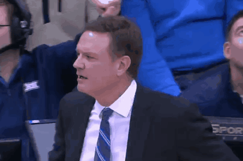 A Man In A Suit And Tie Is Sitting In The Stands Watching A Game GIF