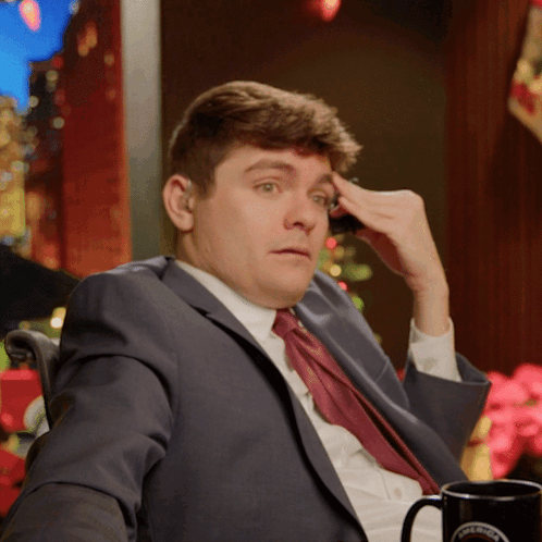 A Man In A Suit And Tie Is Sitting Next To A Coffee Mug That Says Columbia GIF