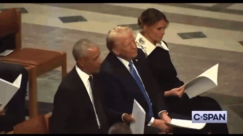 A Man In A Suit And Tie Is Sitting Next To A Woman Holding A Piece Of Paper And A Sign That Says C-Span GIF